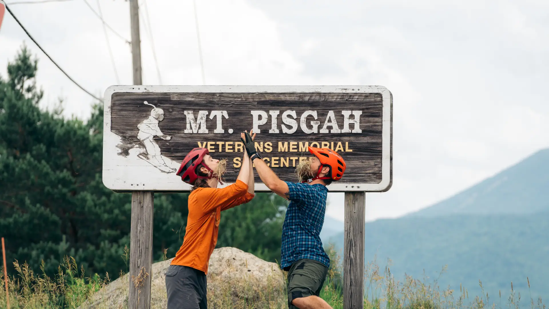 Two mountain bikers being silly in front of the Mt. Pisgah sign