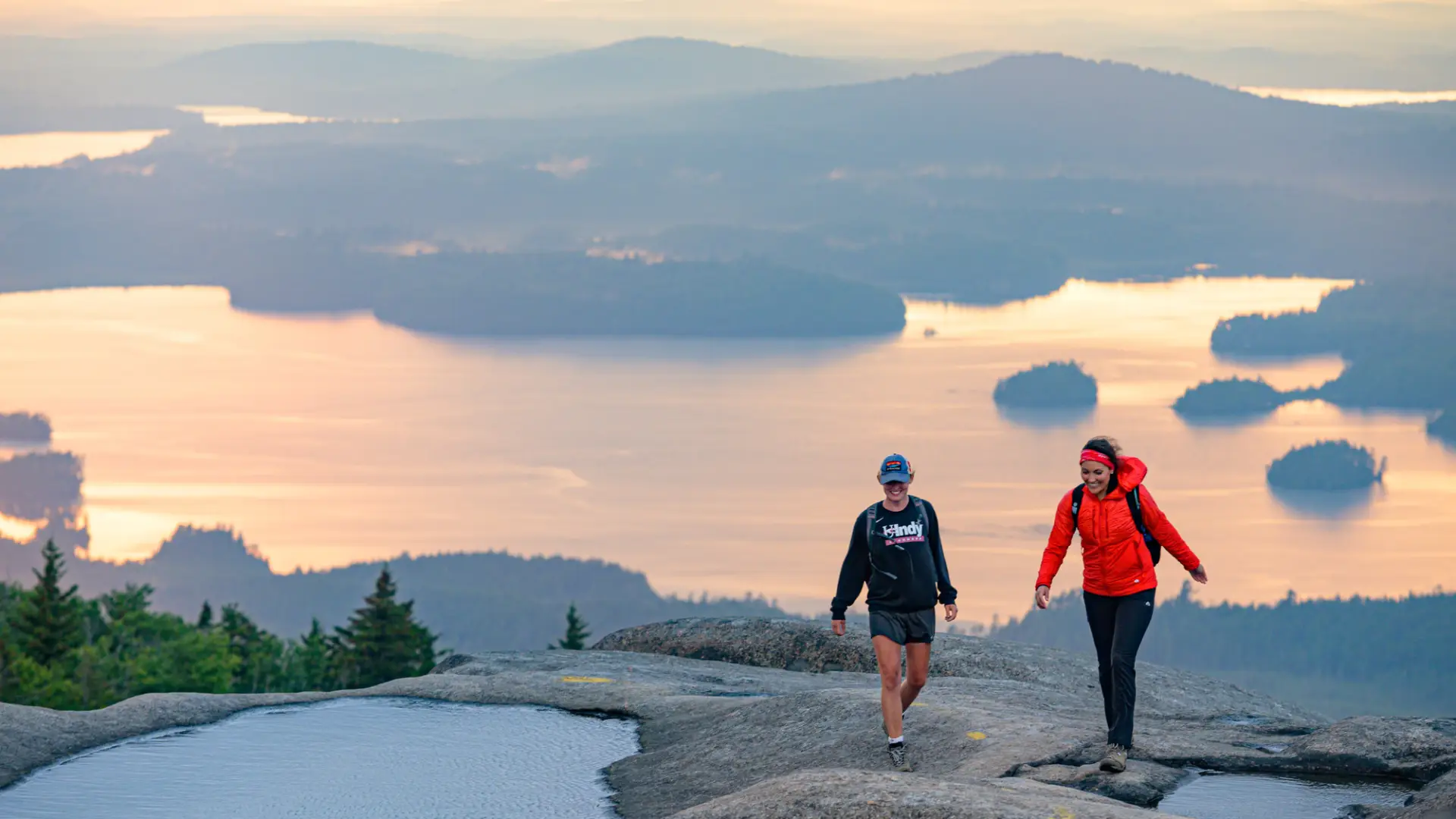 A couple people hiking Ampersand Mountain, a bare rock summit.