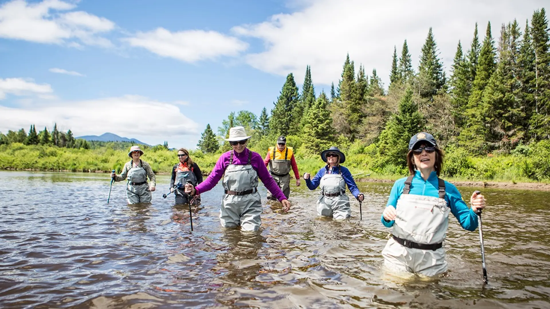 Smiling and laughing people walk the river in chest wadders