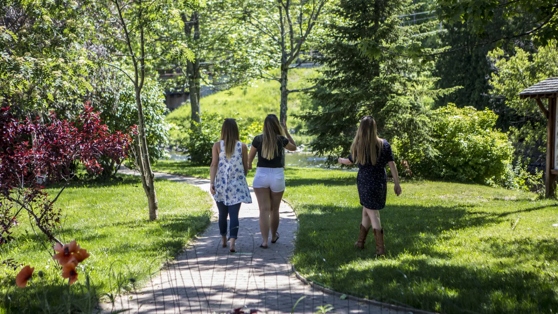 Three girls walk along the stone path of the Saranac Lake Riverwalk on a beautiful summer day.