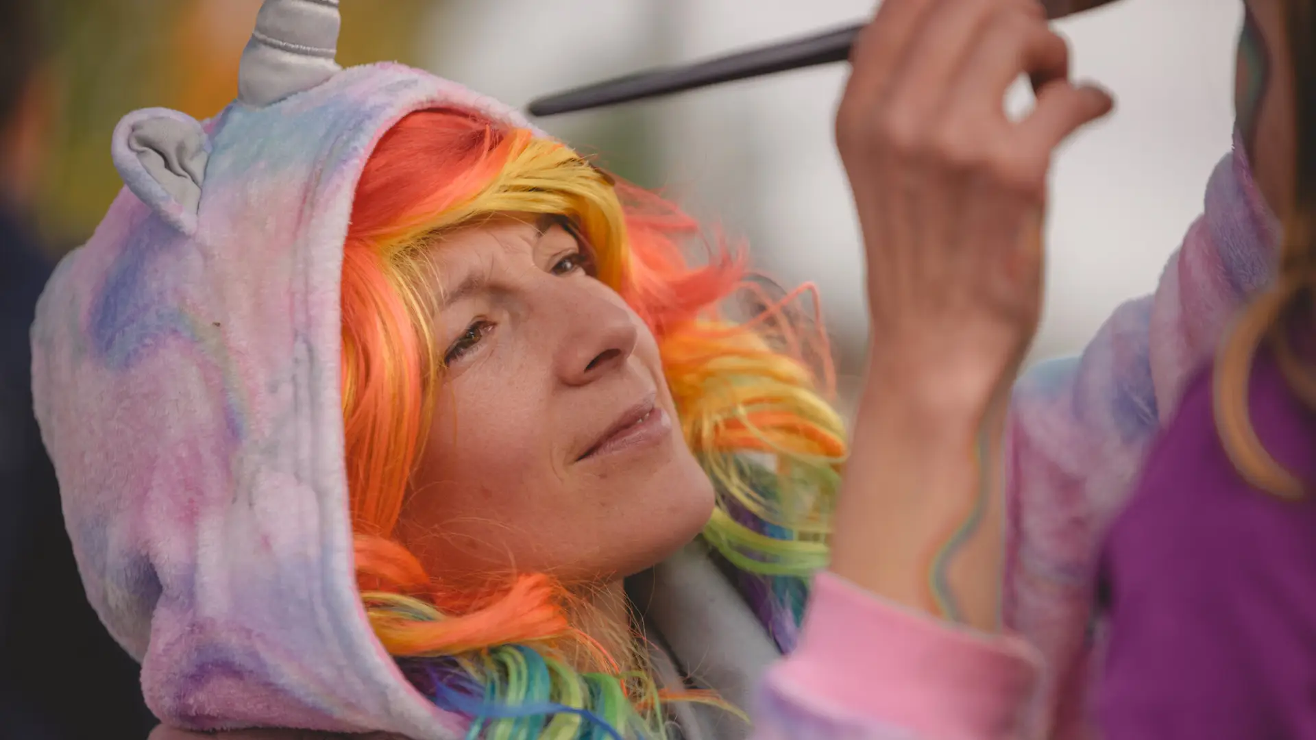 Woman with colorful hair paints a childs face at the fall festival.