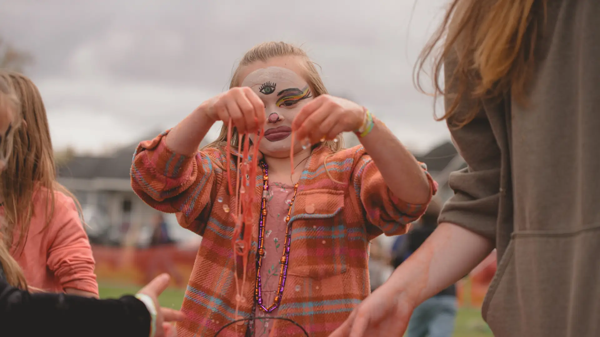 Child with face painted at Tupper's fall festival holds up necklaces.
