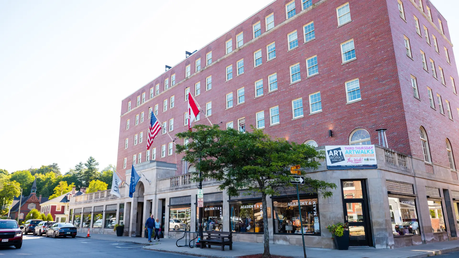The exterior of Hotel Saranac, featuring an American flag and a Canadian flag flying near its stone-arched entrance.