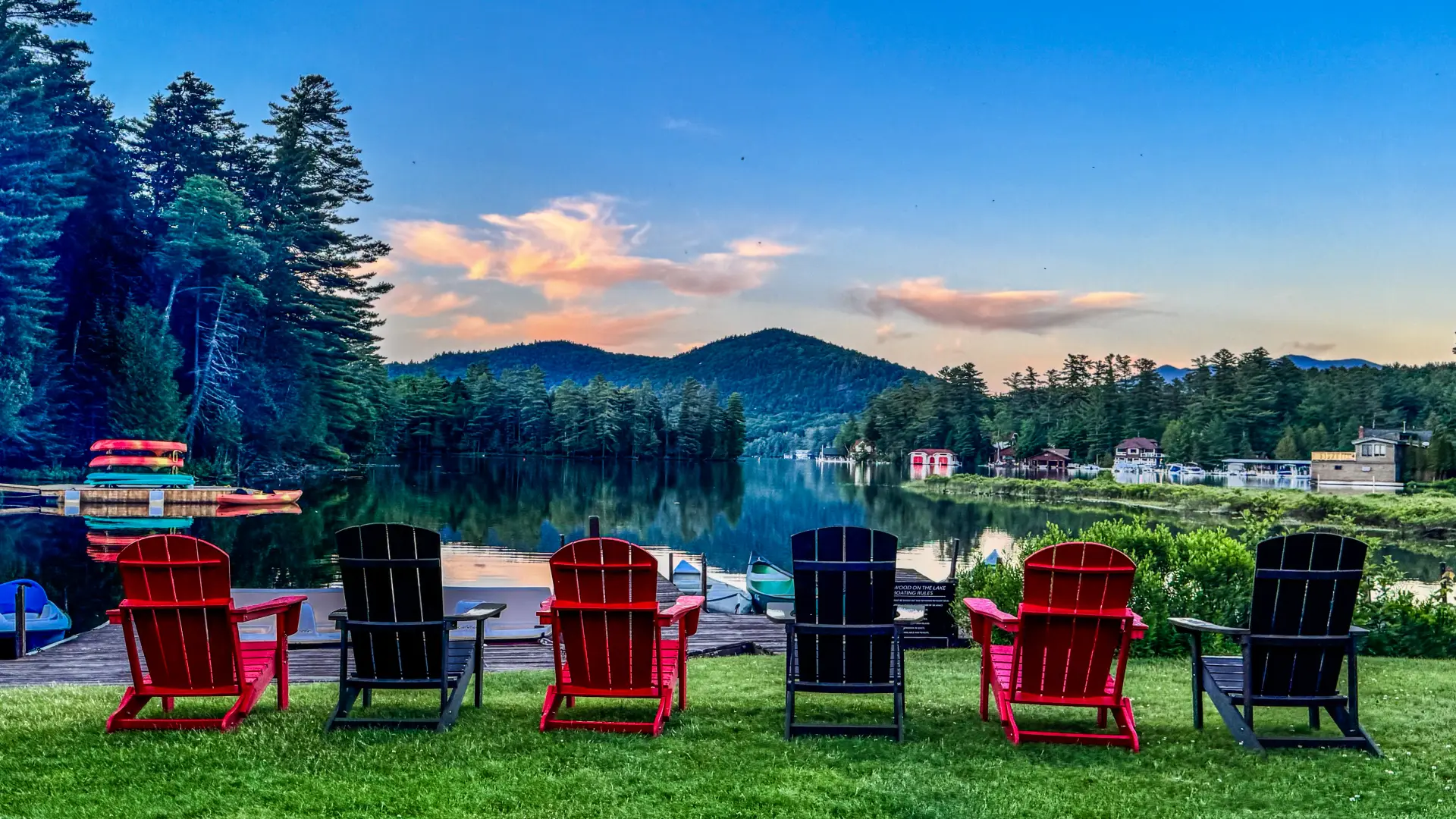 Red and green adirondack chairs by the mirror of the lake and mountains in the distance at Wildwood on the Lake.