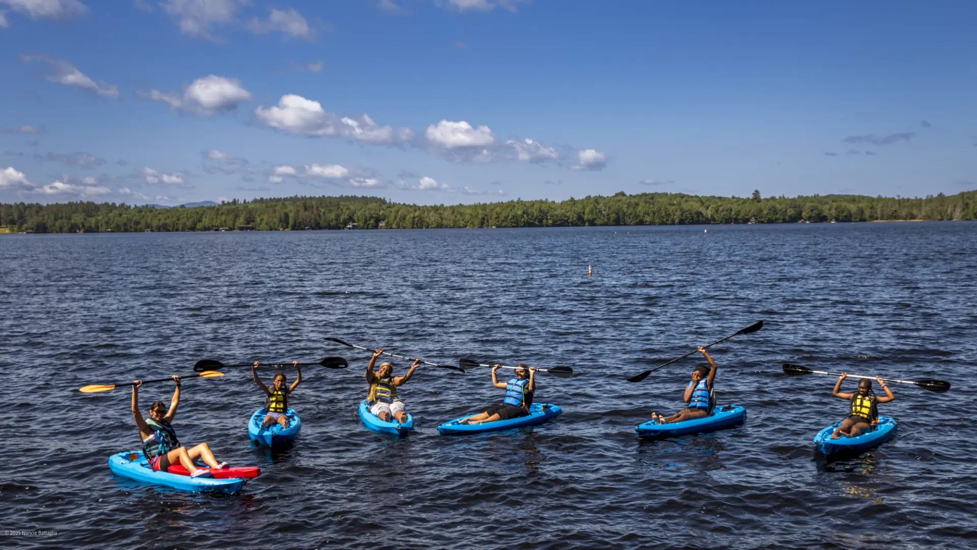 A group of kayakers hold their paddles above their heads in triumph.