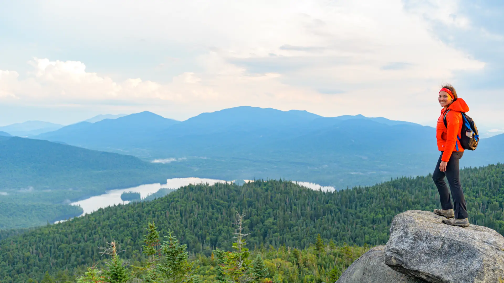 A smiling young woman stares off the top of Ampersand Mountain