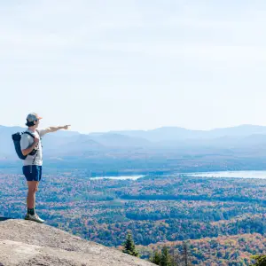 A man points to a mountain range covered in foliage in the fall.