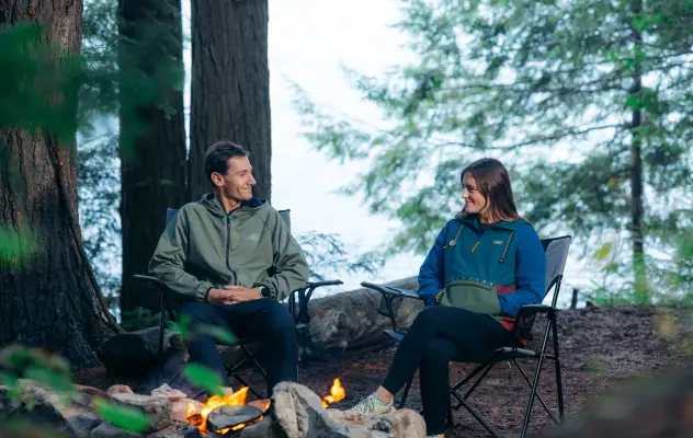 A man and woman sit at a campsite. 