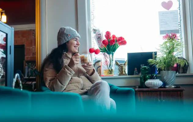 A woman in a beanie and jacket enjoys coffee  in a coffee shop. 