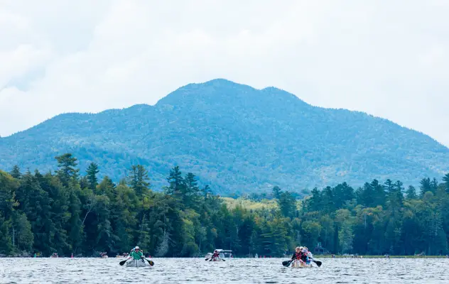 A group of people paddle in canoes on a lake. 