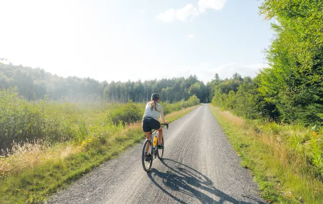 A cyclist rides on a gravel trail on a sunny summer day.