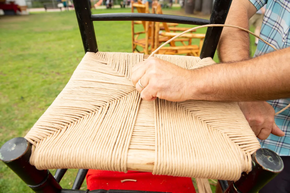 A man winds straw around a chair. 