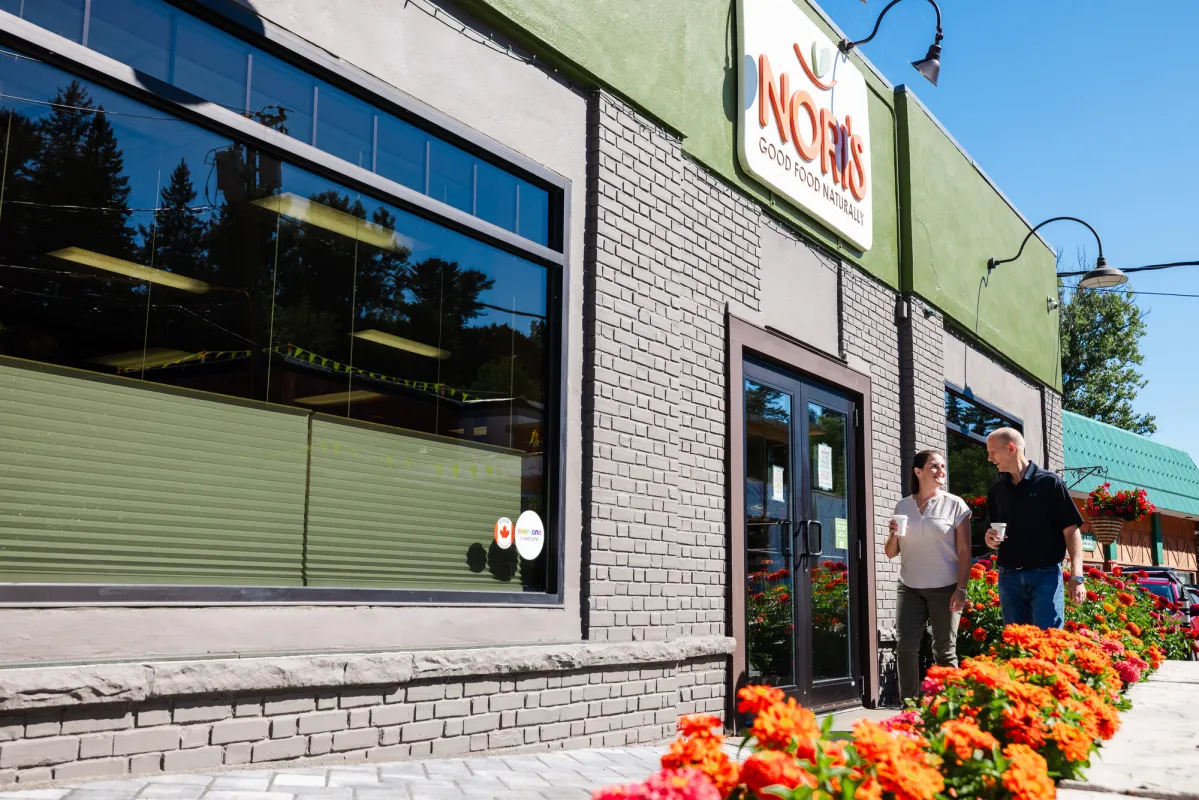 A man and woman walk with coffee cups to a health food store. 