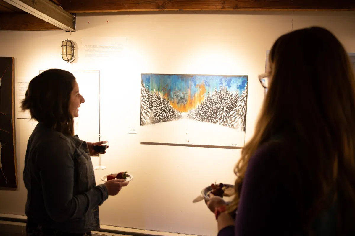 Two women discuss a painting in an art gallery.