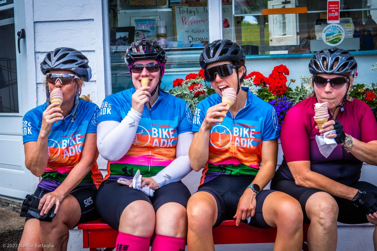 A group of cyclists eat ice cream outside of an ice cream shop.