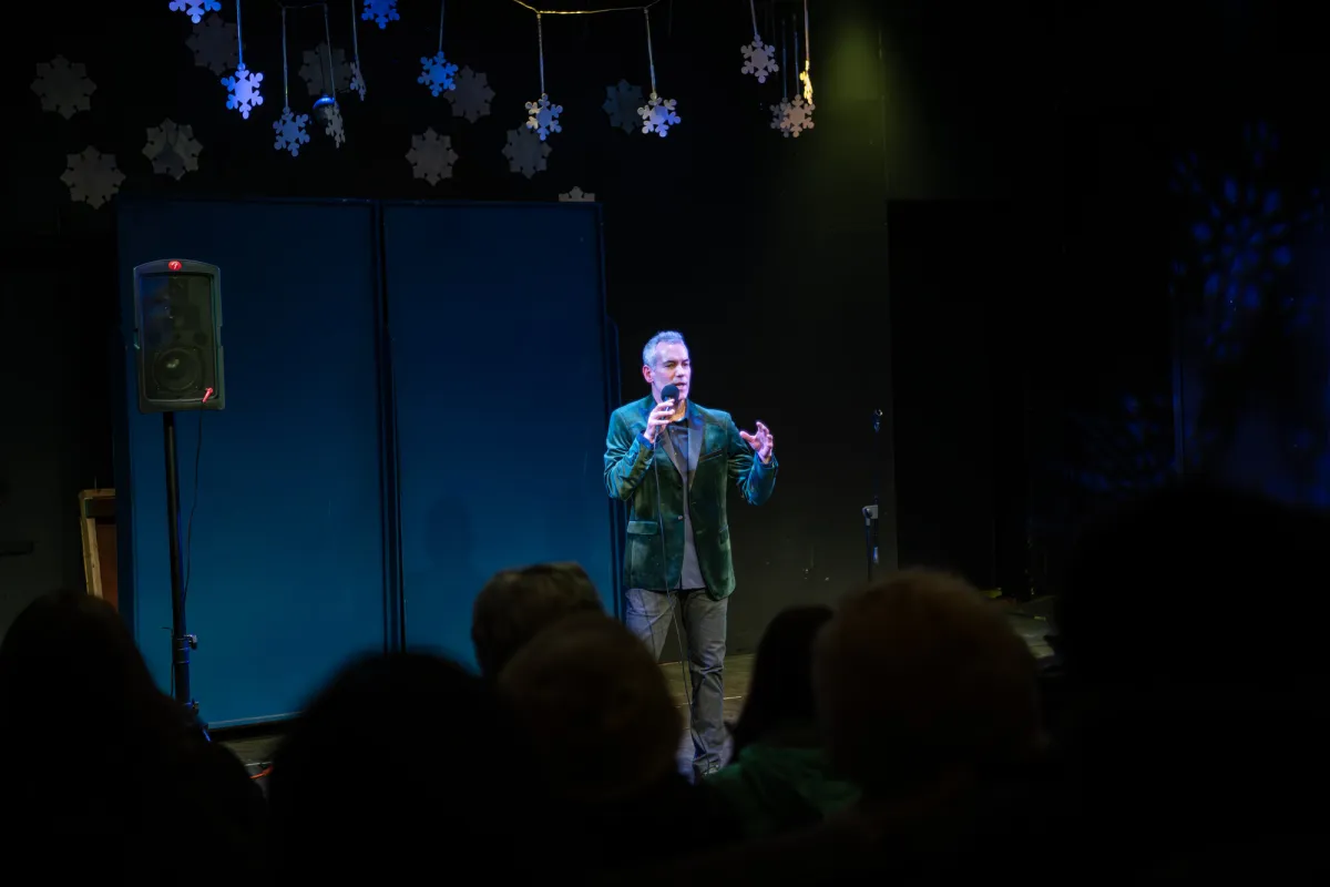 A man in a green jacket sings for an audience.