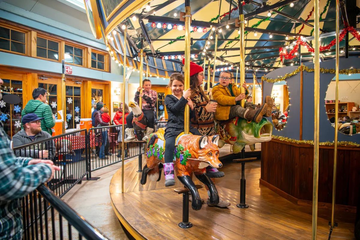 Young children ride on an indoor carousel in winter.