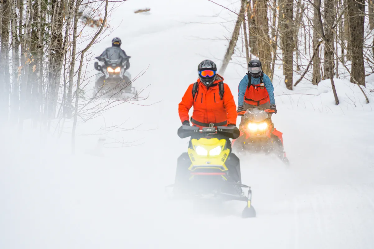 A group of snowmobilers ride on a snowy trail.