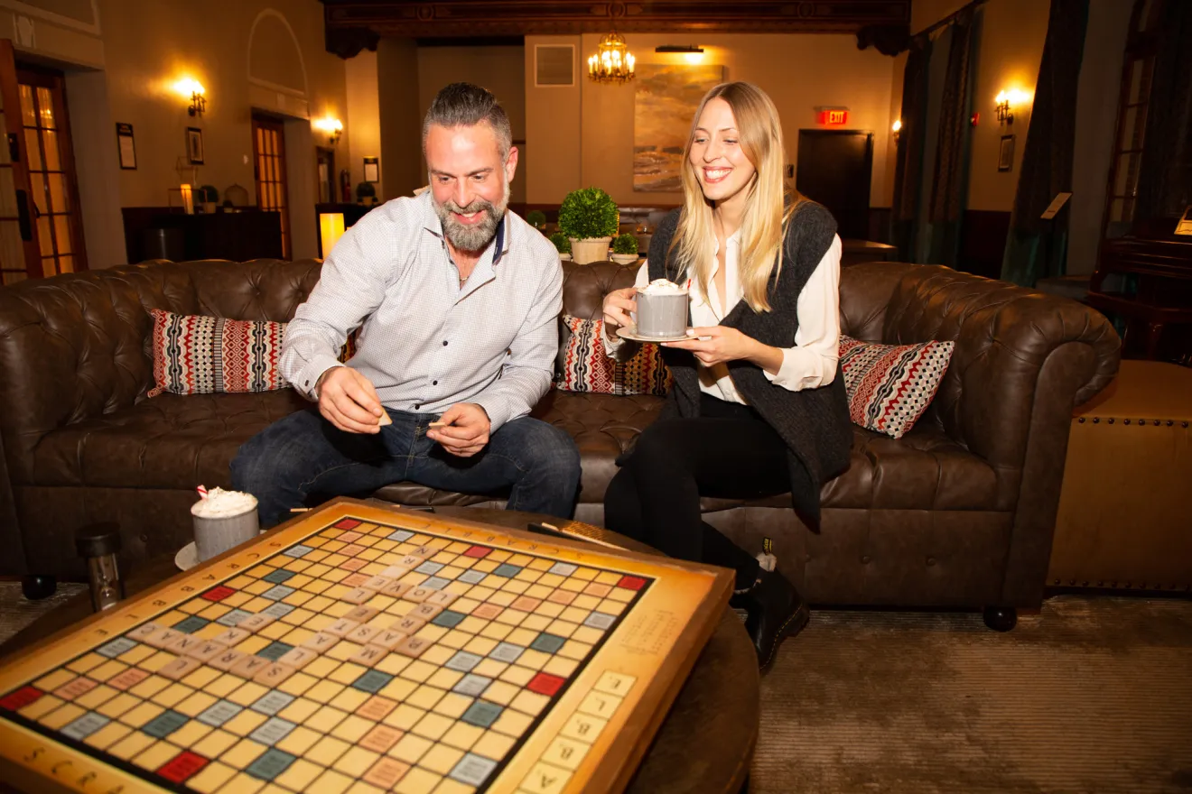 A man and woman play scrabble in a hotel lobby. 