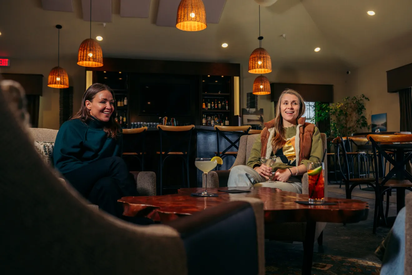 Three women share drinks together at a coffee table in a restaurant.
