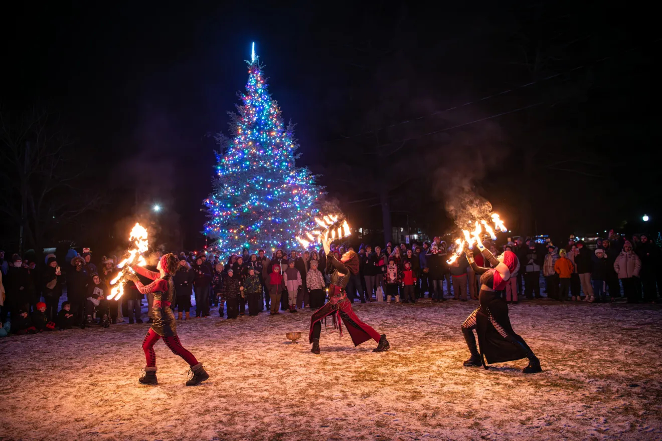 Women dance with fire sticks in front of a crowd at a nighttime Christmas event.