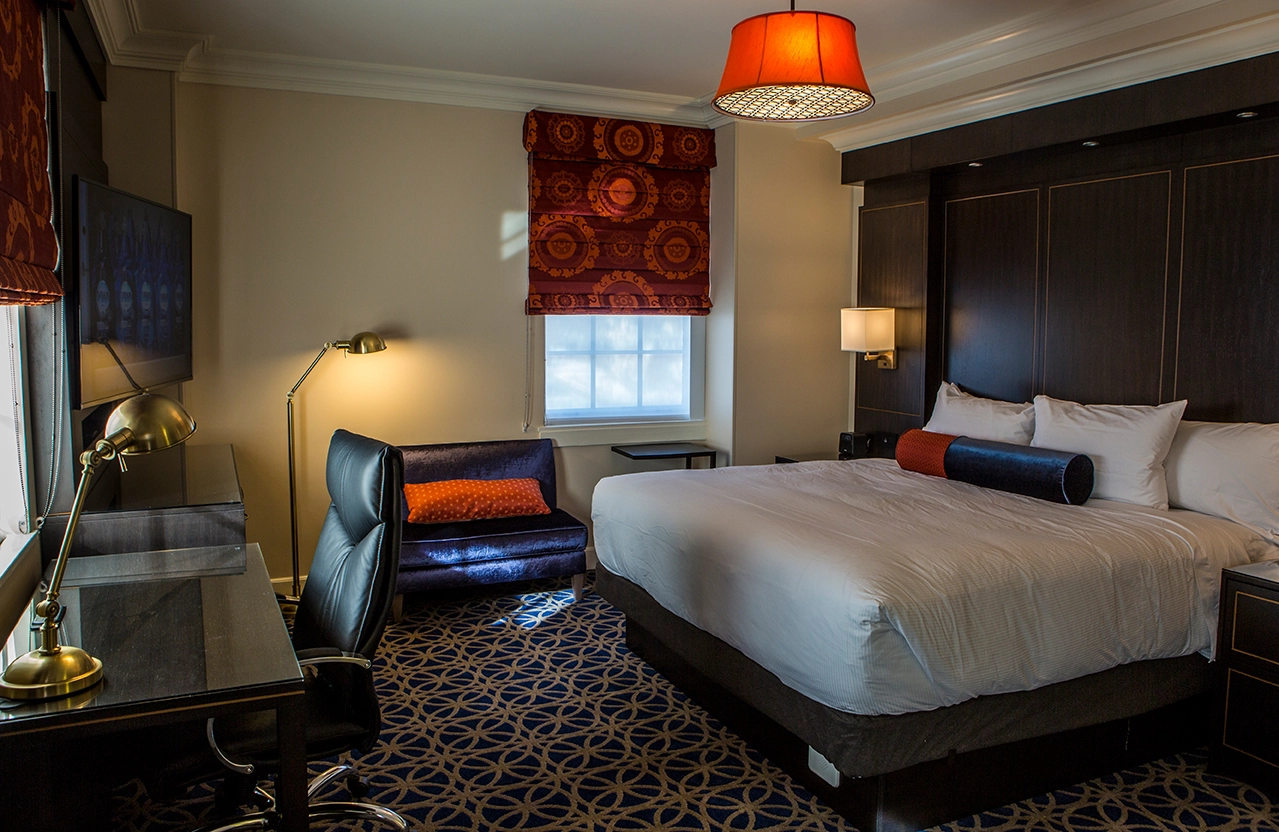 A hotel room interior, featuring large bed, modern-style desk, and retro lamp over the bed.