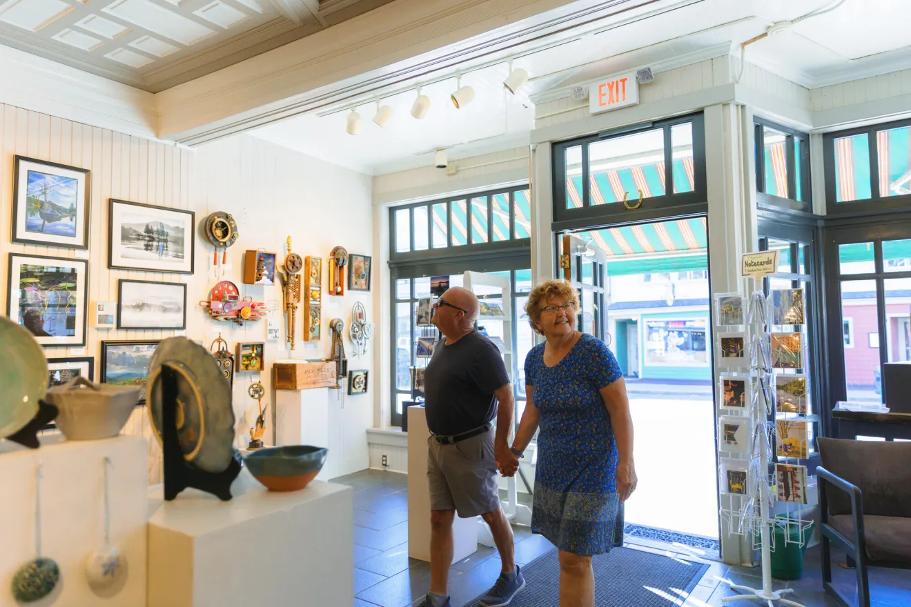 A man and woman walk into an art gallery on a sunny day. 