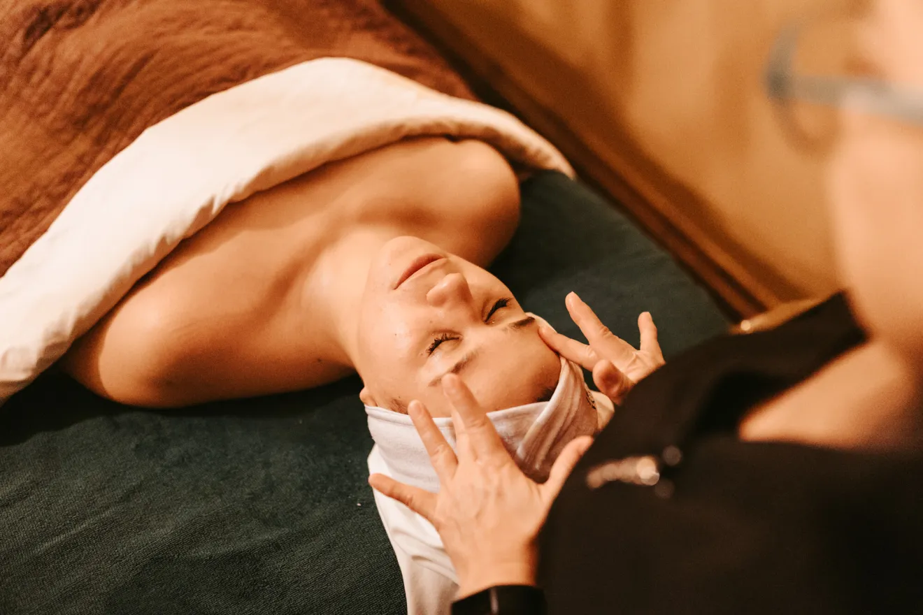 A woman gets a facial at a spa while wrapped in a towel. 
