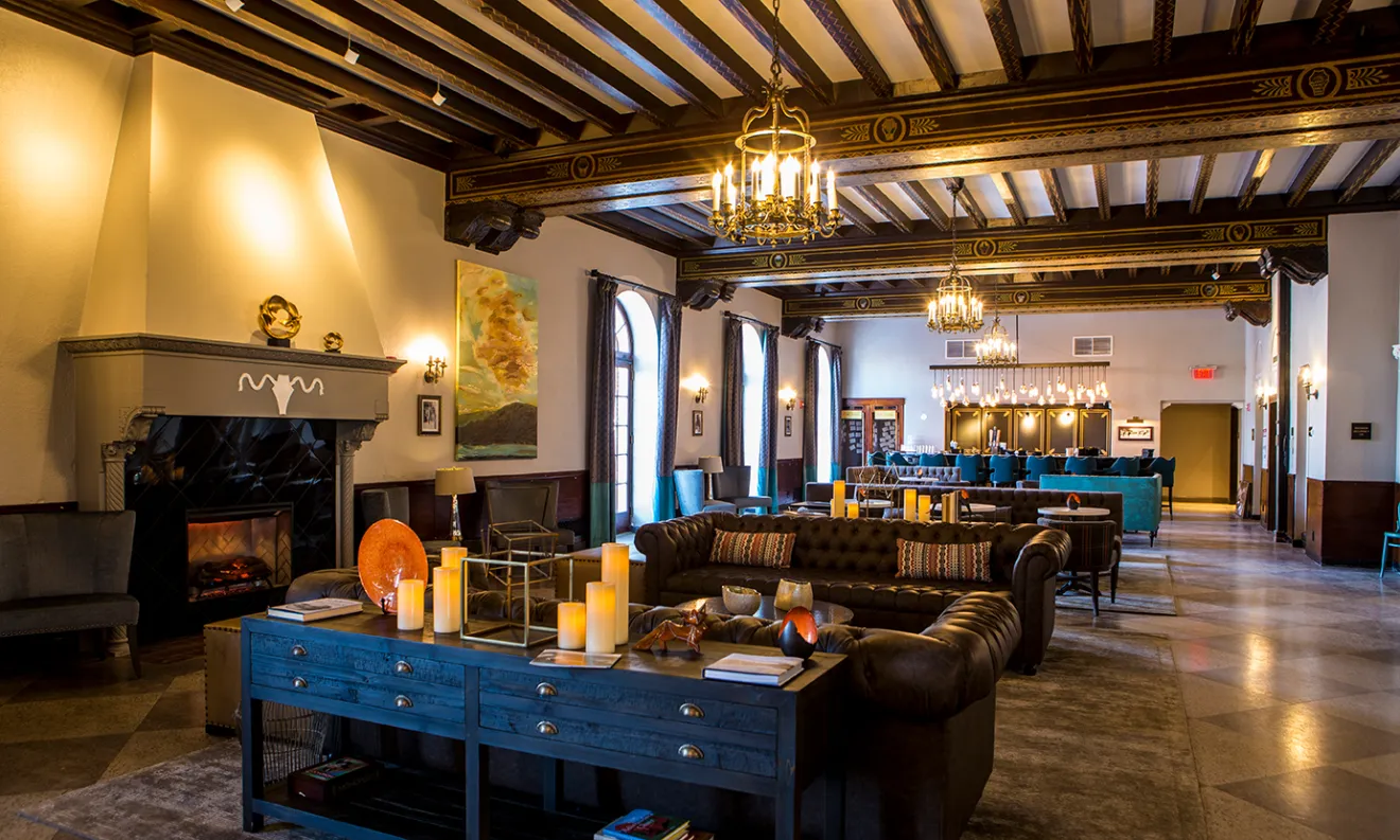 A hotel bar features modern, luxurious 1920s-style furnishings, as well as chandeliers and a fireplace.
