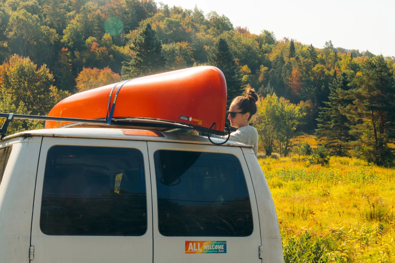 A person strapping a canoe to a van.