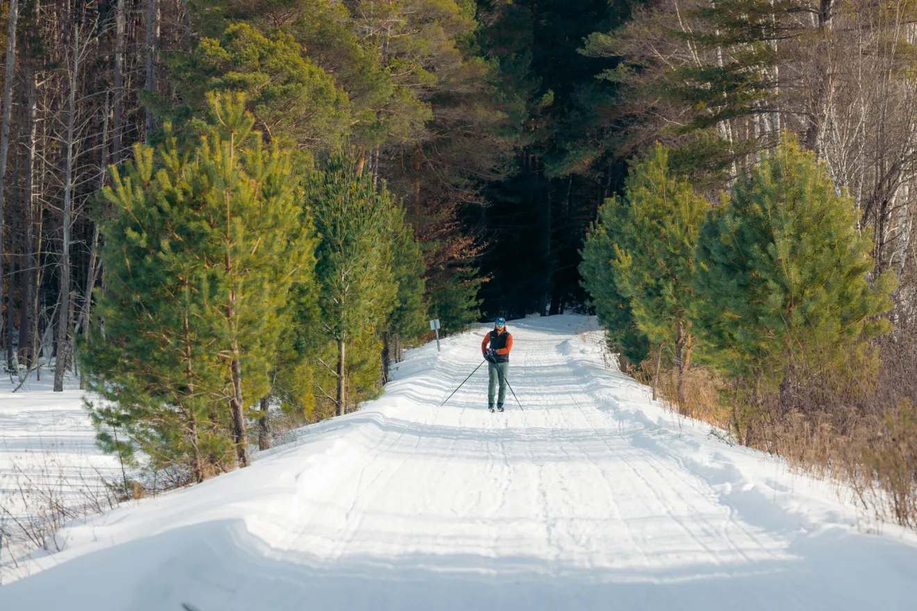 A man cross-country skis on a wide snowy path in winter.