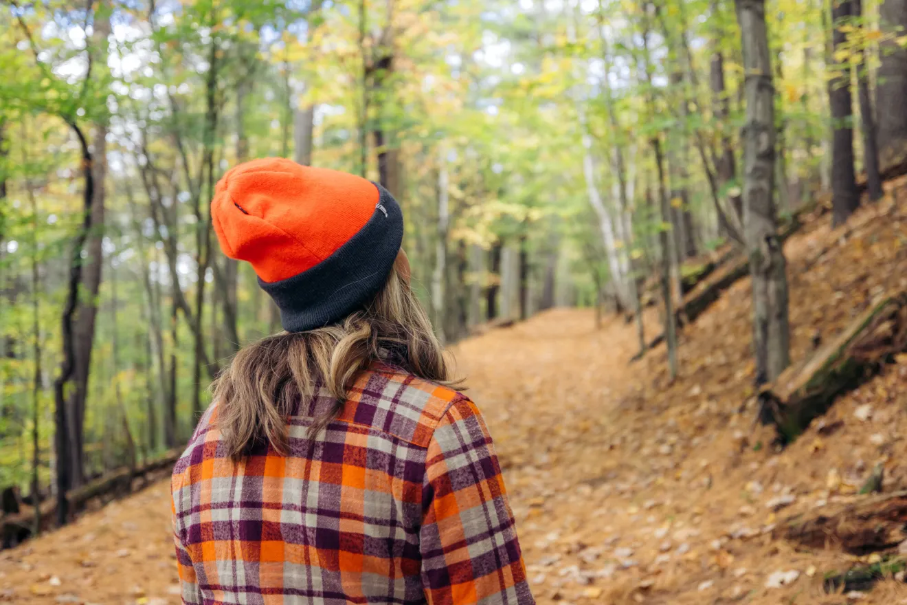 A woman looks to a fall trail while wearing bright orange. 