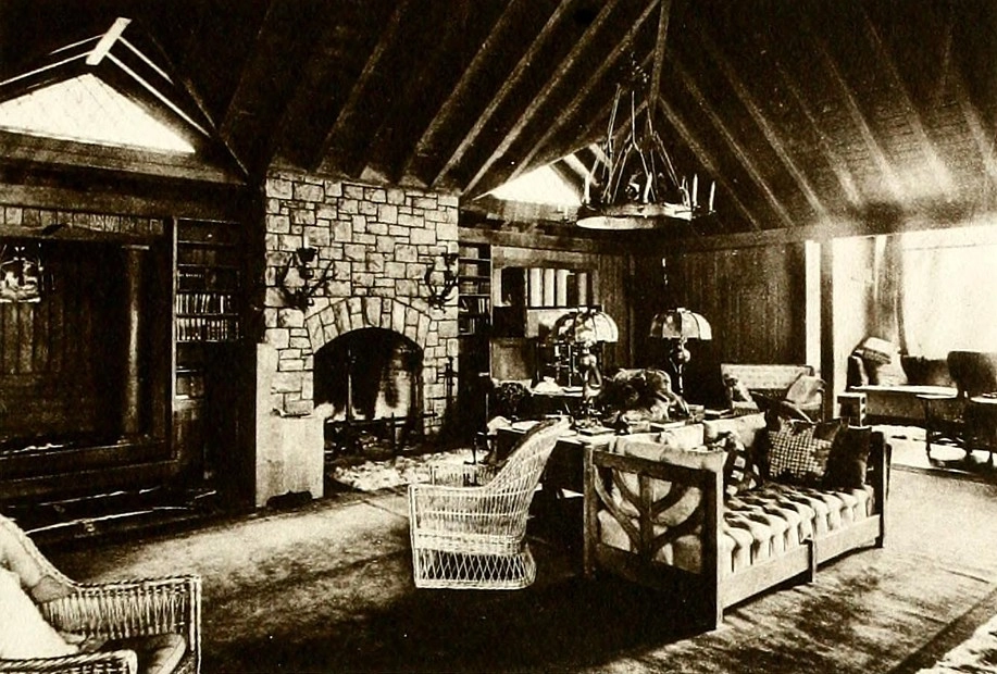 A vintage black and white image of a lavish, rustic Adirondack Great Camp living room, with stone fireplace.