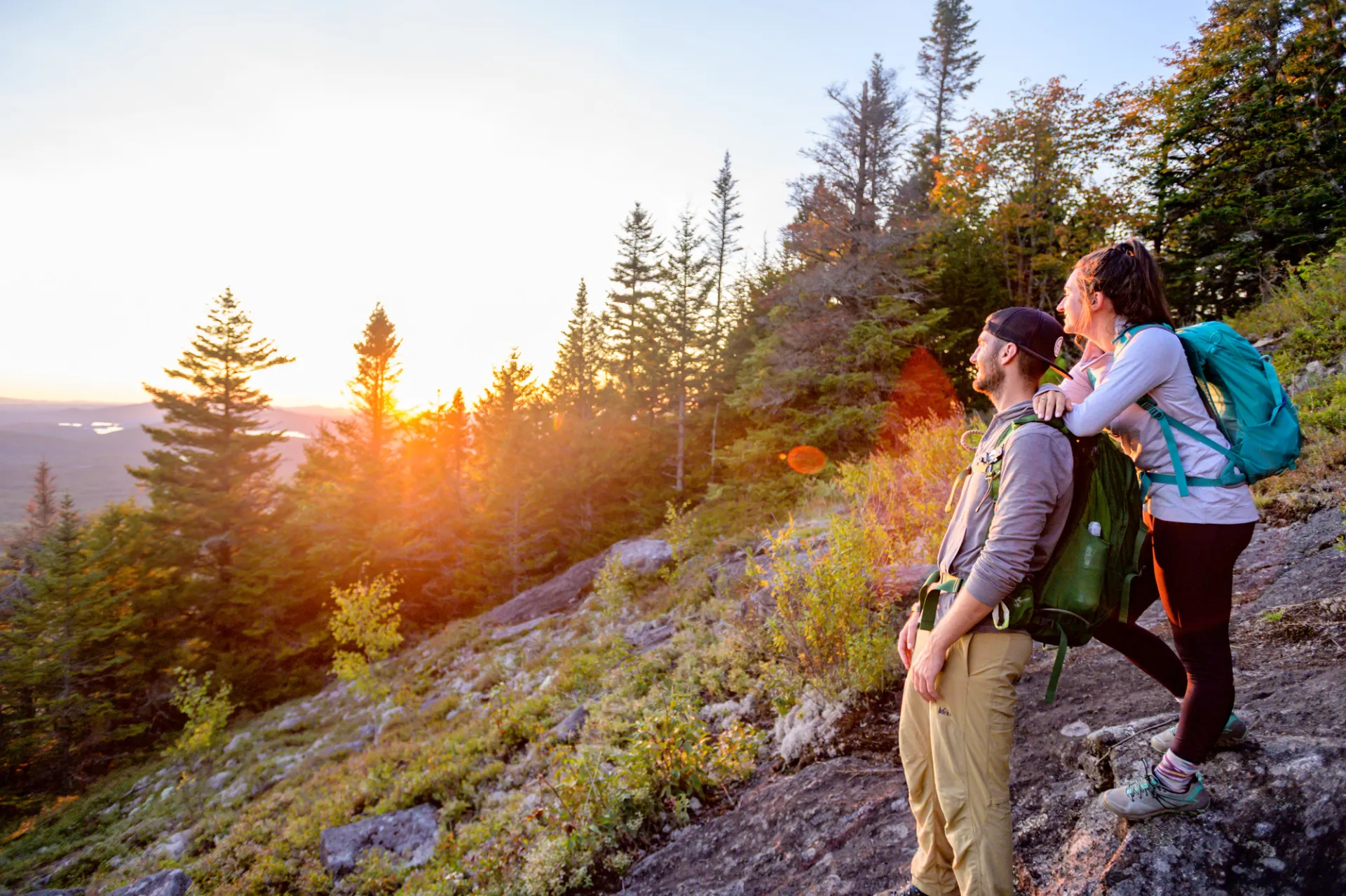 A man and woman watch a sunset from a mountain top.