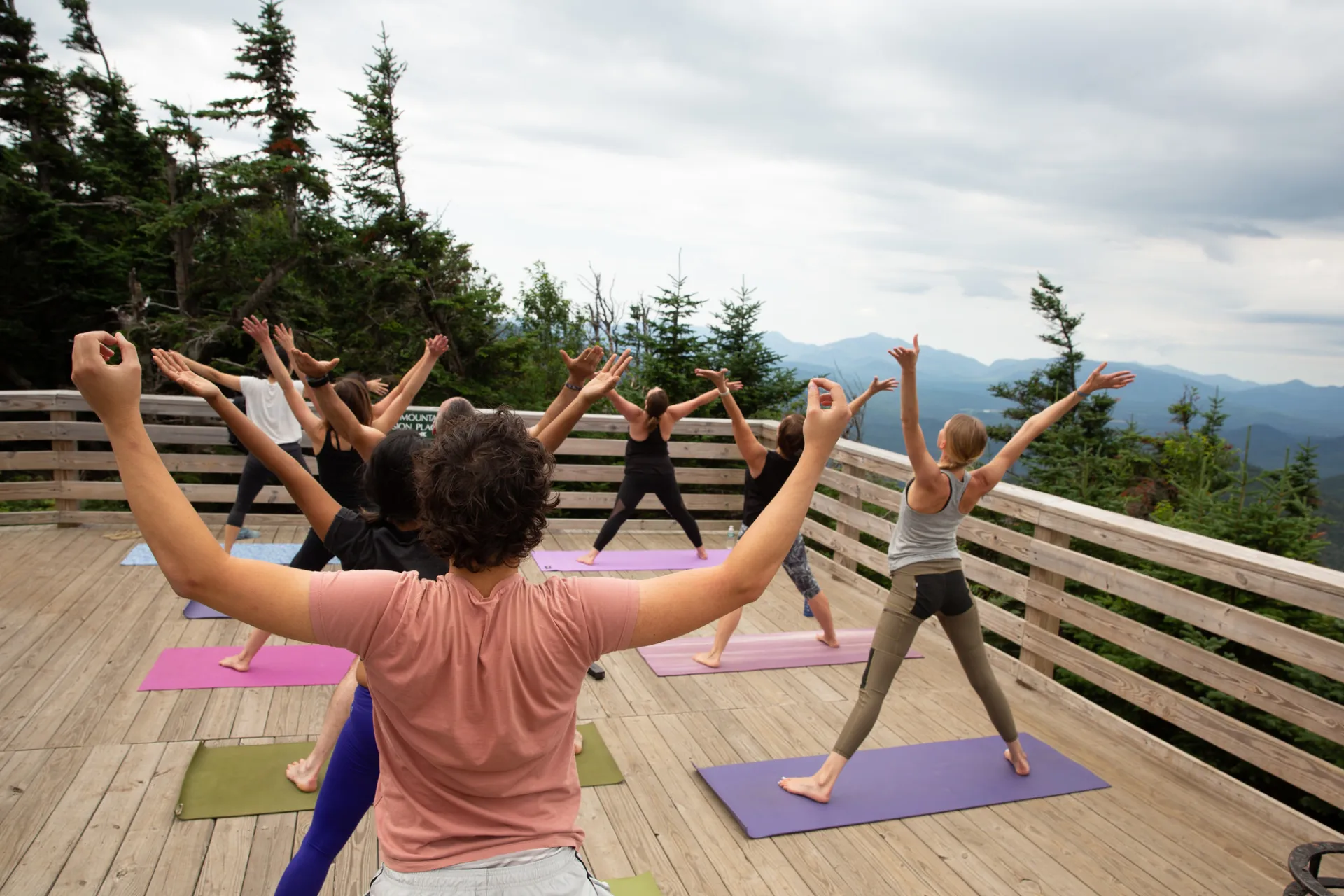 A group of women do yoga on a porch overlooking a mountain range. 