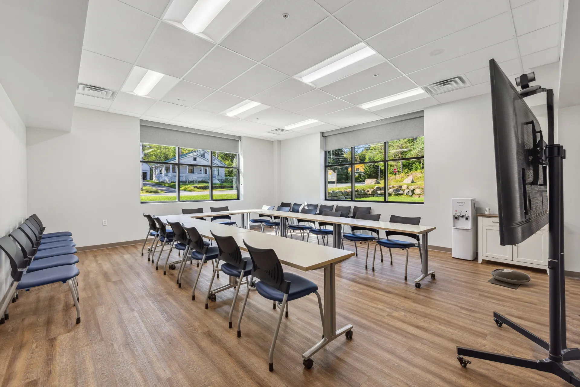 The meeting space arranged in a U shape with chairs and a large screen on a mount, viewed from the doorway.