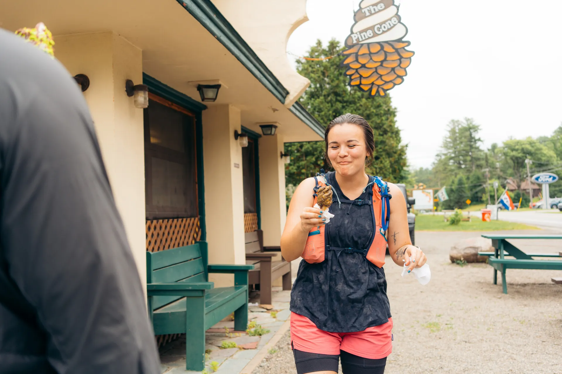 A woman eats an ice cream cone while in biking gear at a roadside ice cream stop.