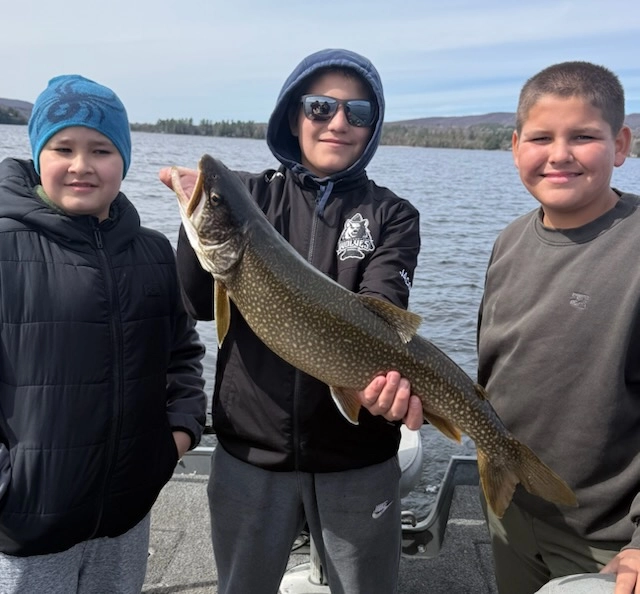 Three kids hold a fish and smile at the camera