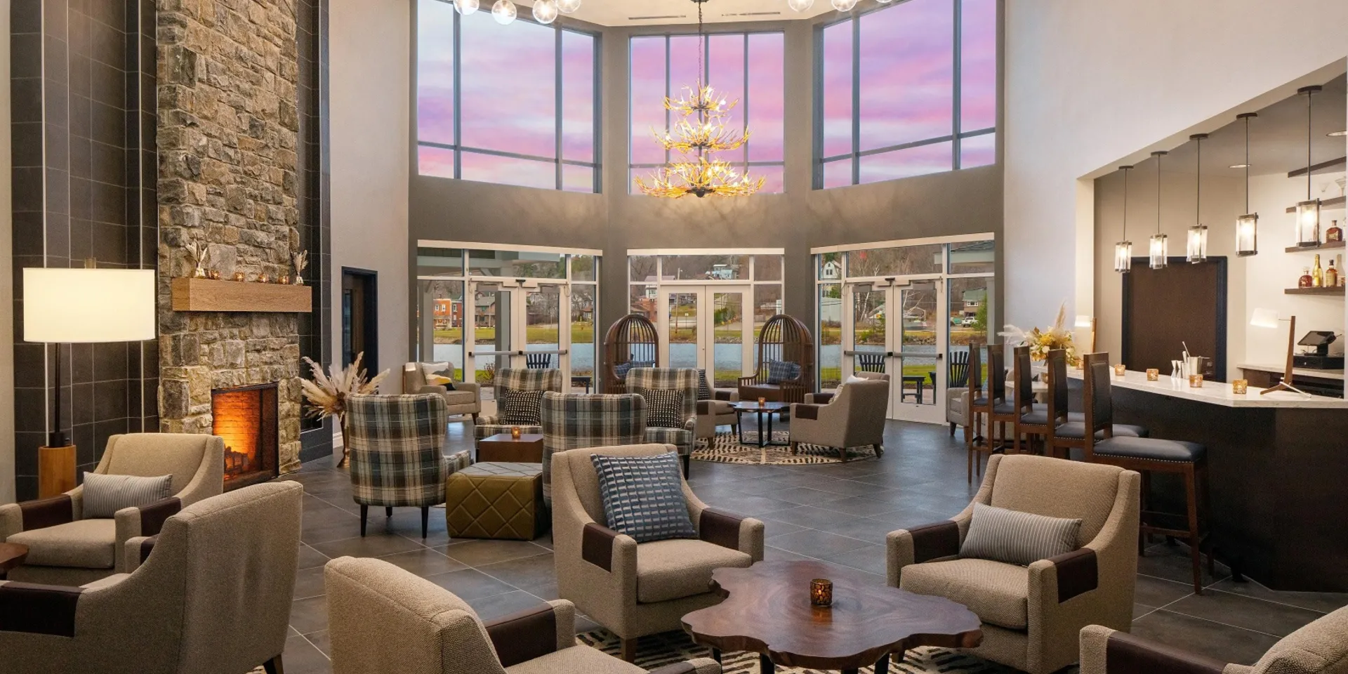 Grand lobby space with stone fireplace, plush armchairs and a view of the lake and mountains