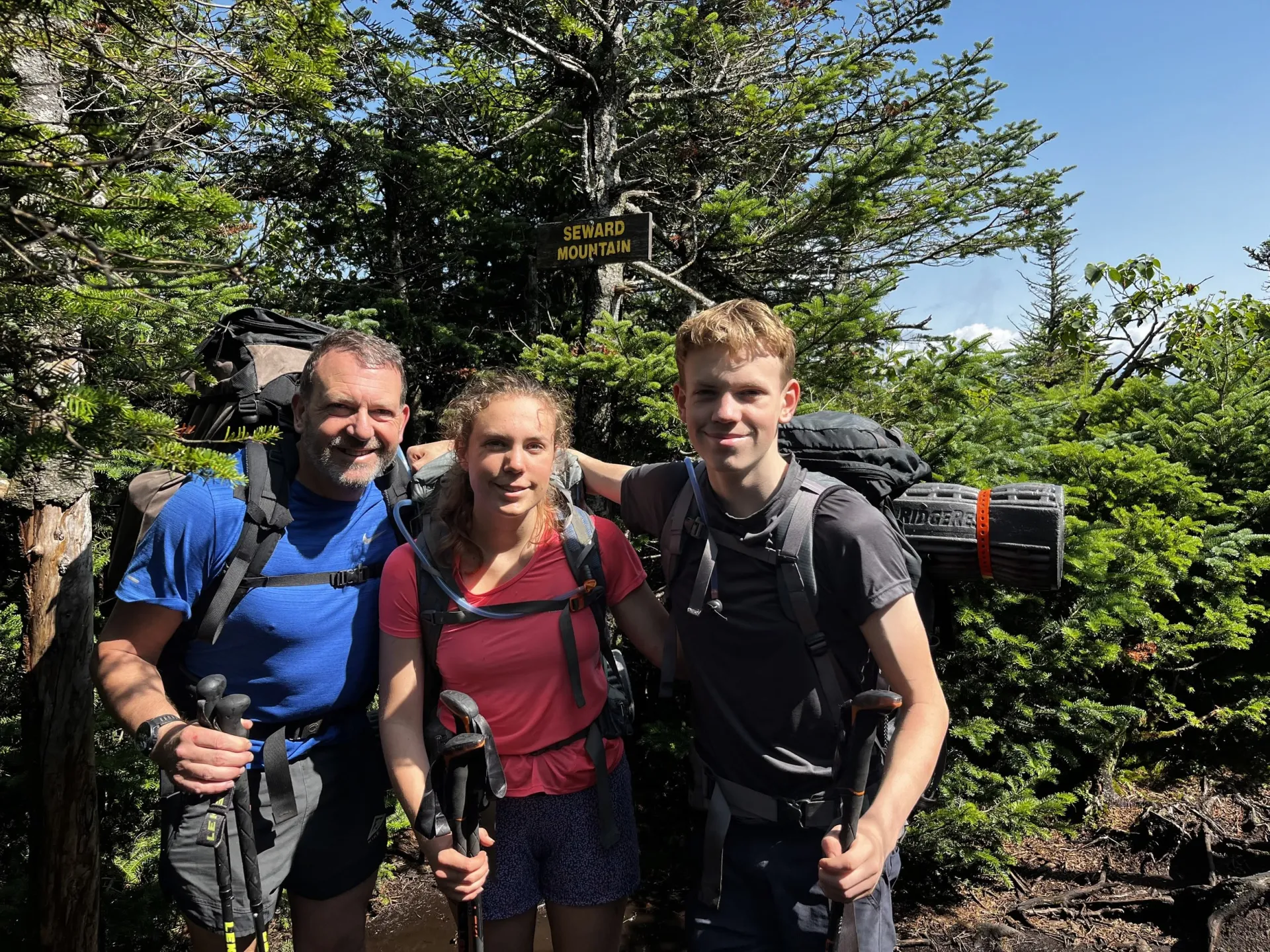 A group smiles with their camping gear at the summit of Seward Mountain