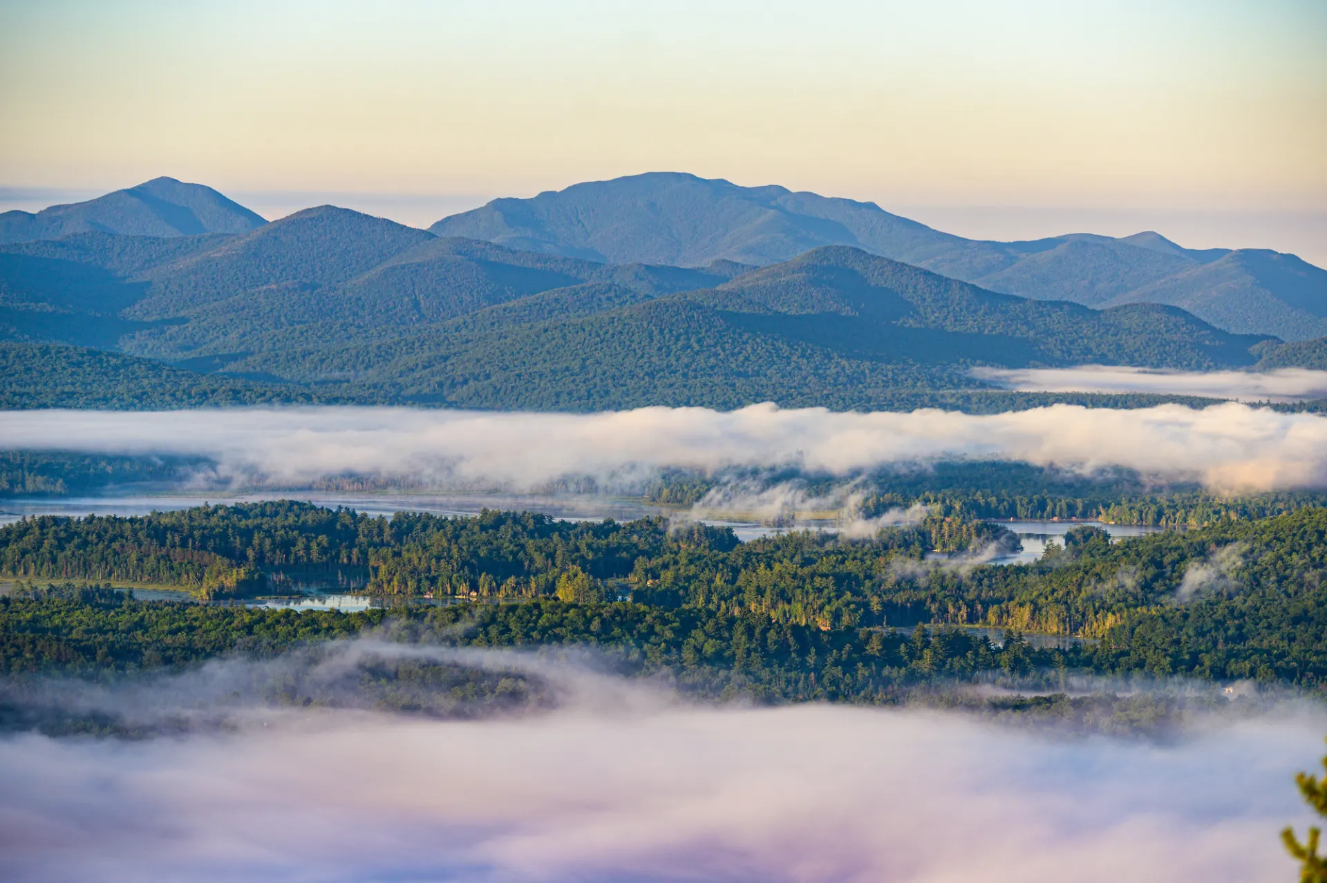 A wide view of a misty valley and mountains at sunrise in the Adirondack Mountains.