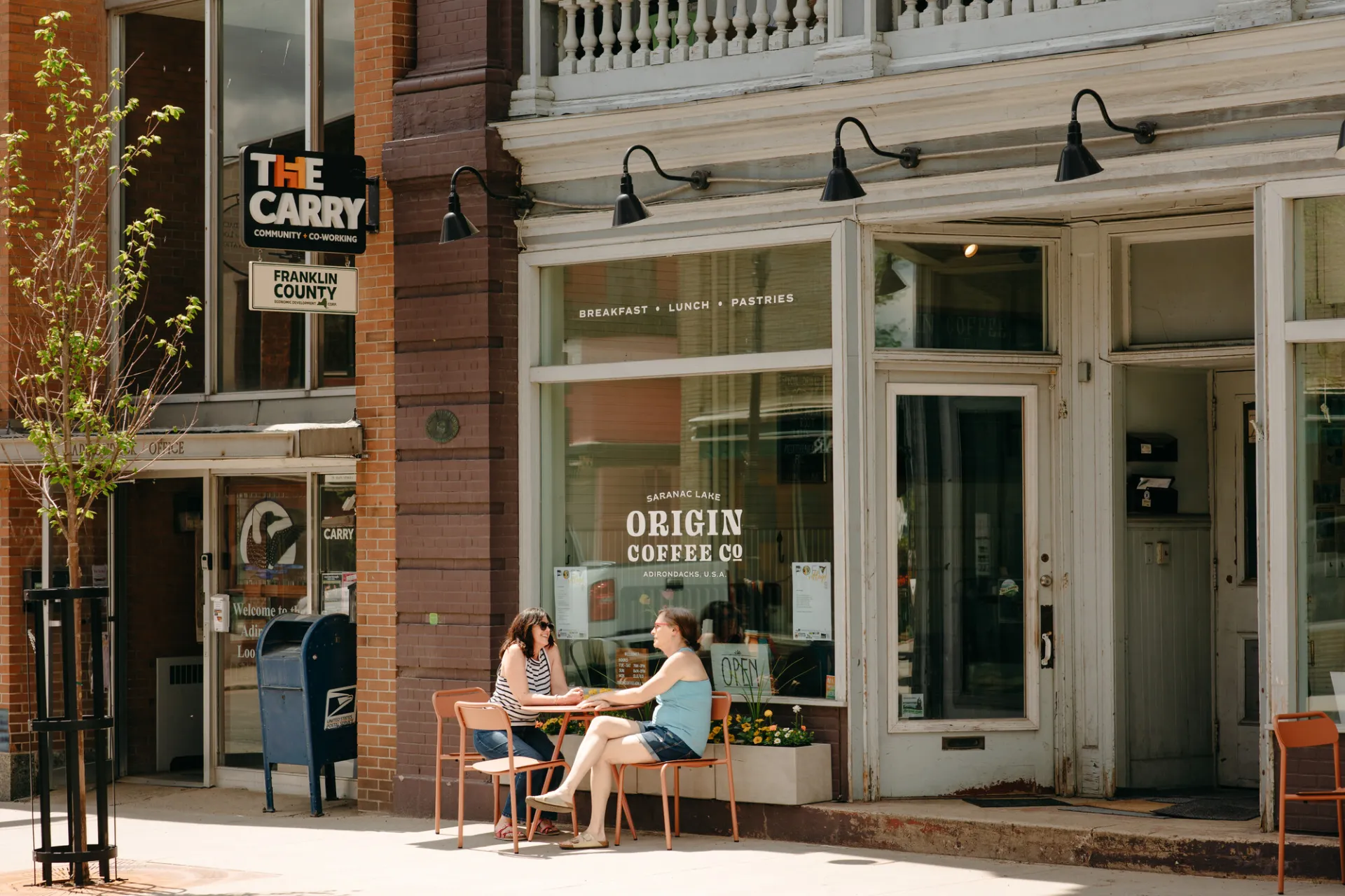 two women drink coffee outside a coffee shop.