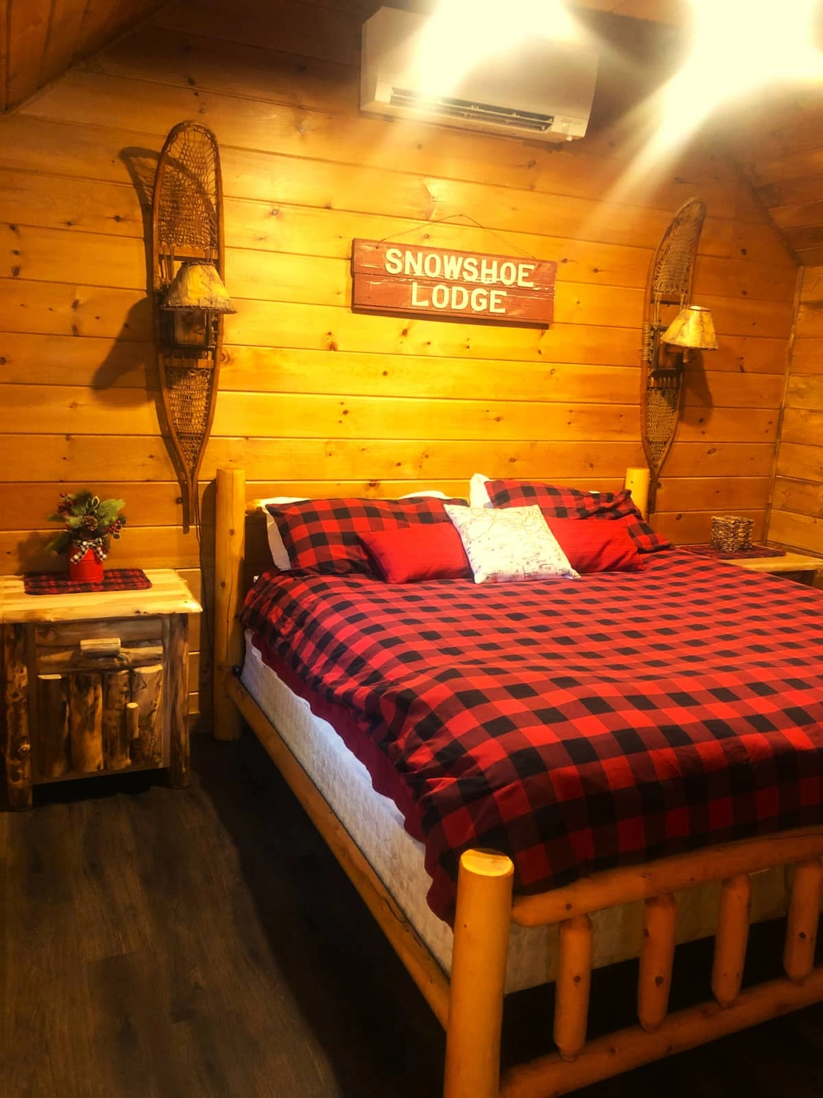 A bedroom with knotty pine paneling, snowshoe sconces and buffalo plaid style bedding.