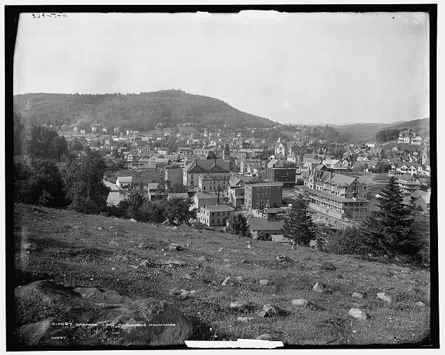 A vintage black and white image looking down from a hill on a small town.