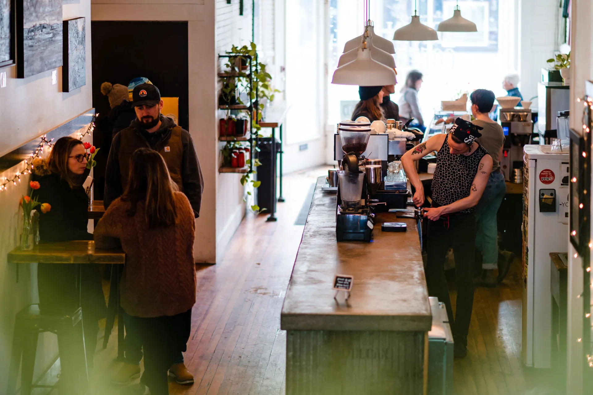 Barista prepares to pull a freshly ground espresso shot on a live edge bar while patrons mingle.