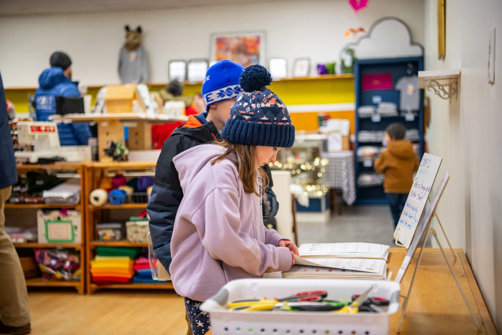 A young girl and boy pick up supplies from an art station at a craft store.