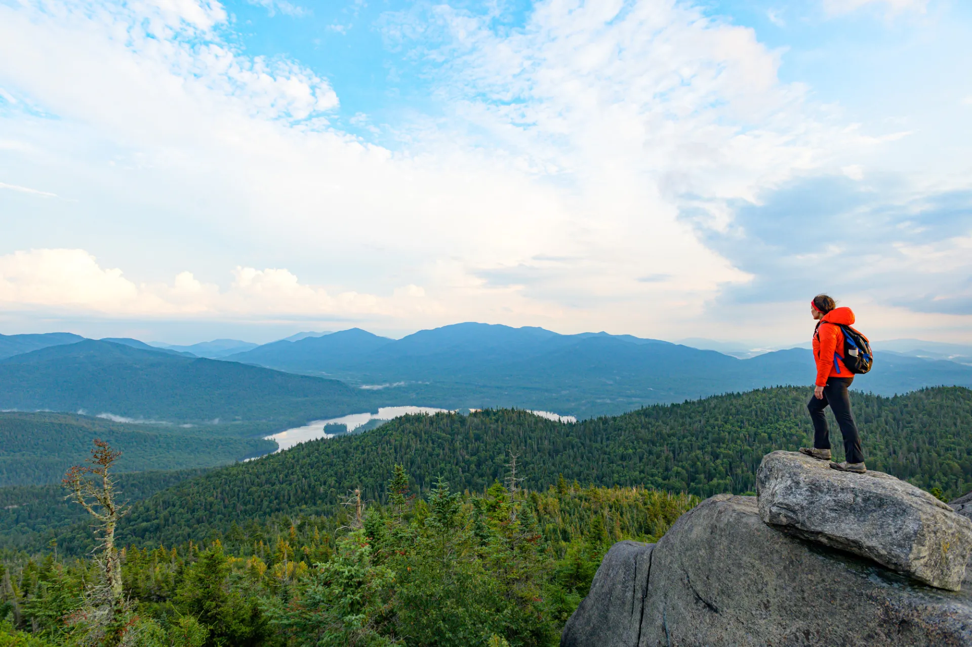 A woman stands on a rock overlooking a mountain range.