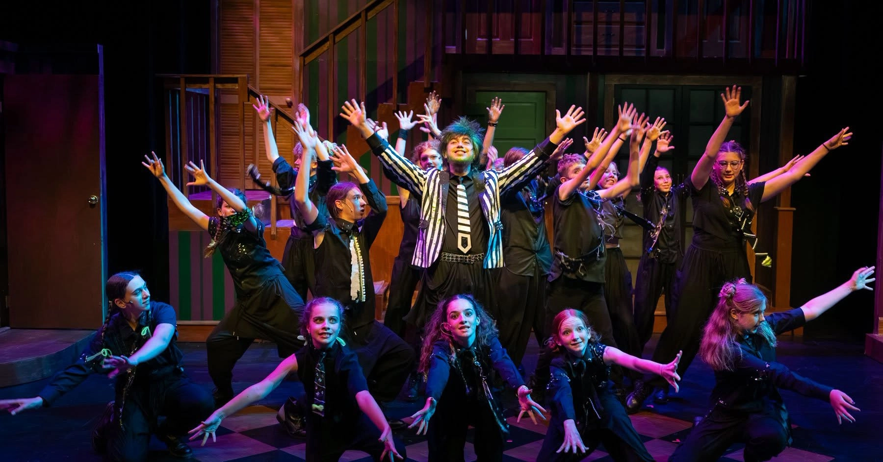 A cast of performers in costume, posing at the end of a musical number with their arms outstretched.