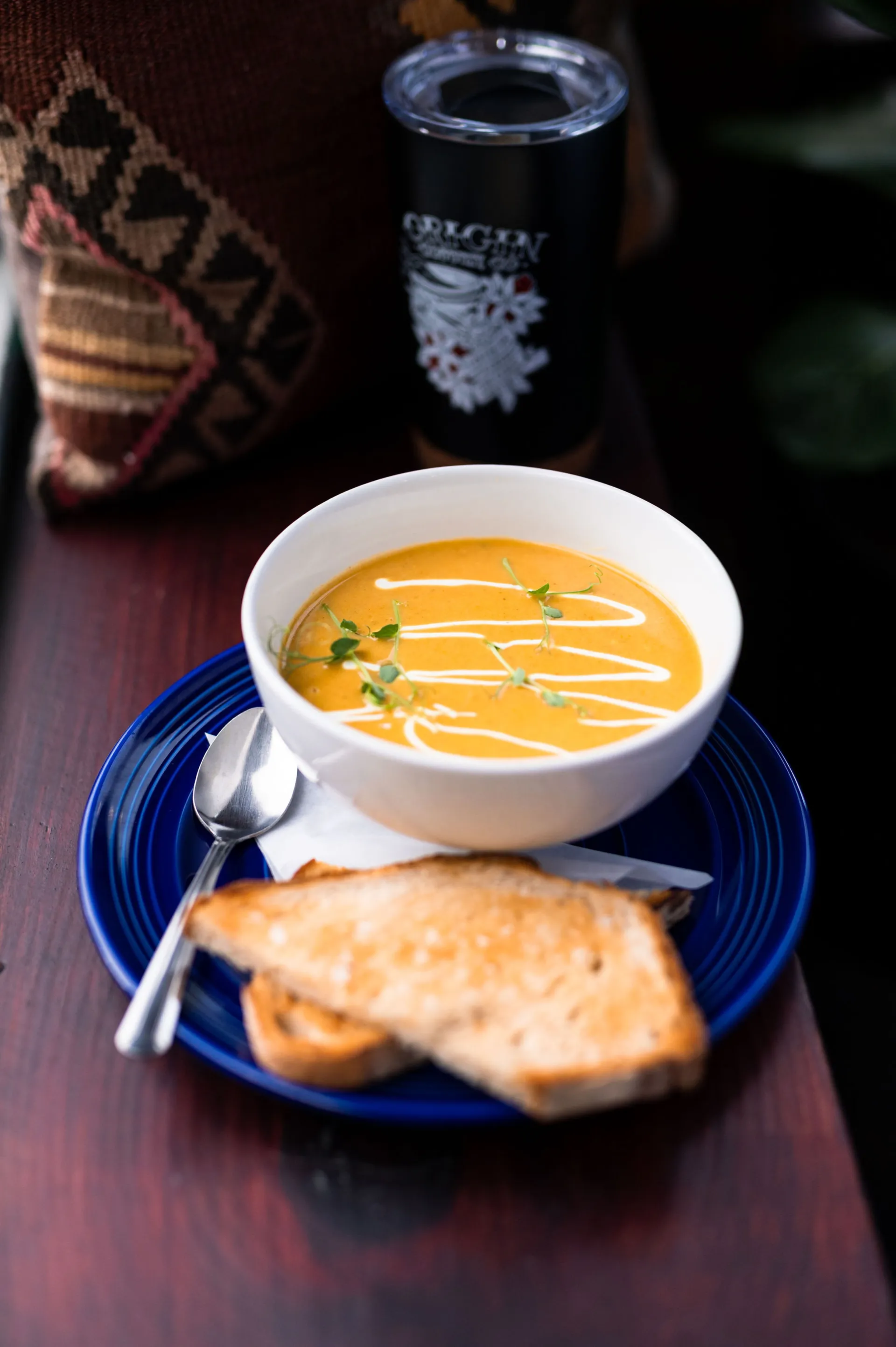 Creamy squash soup in a white bowl with toasted bread on a blue plate with spoon.