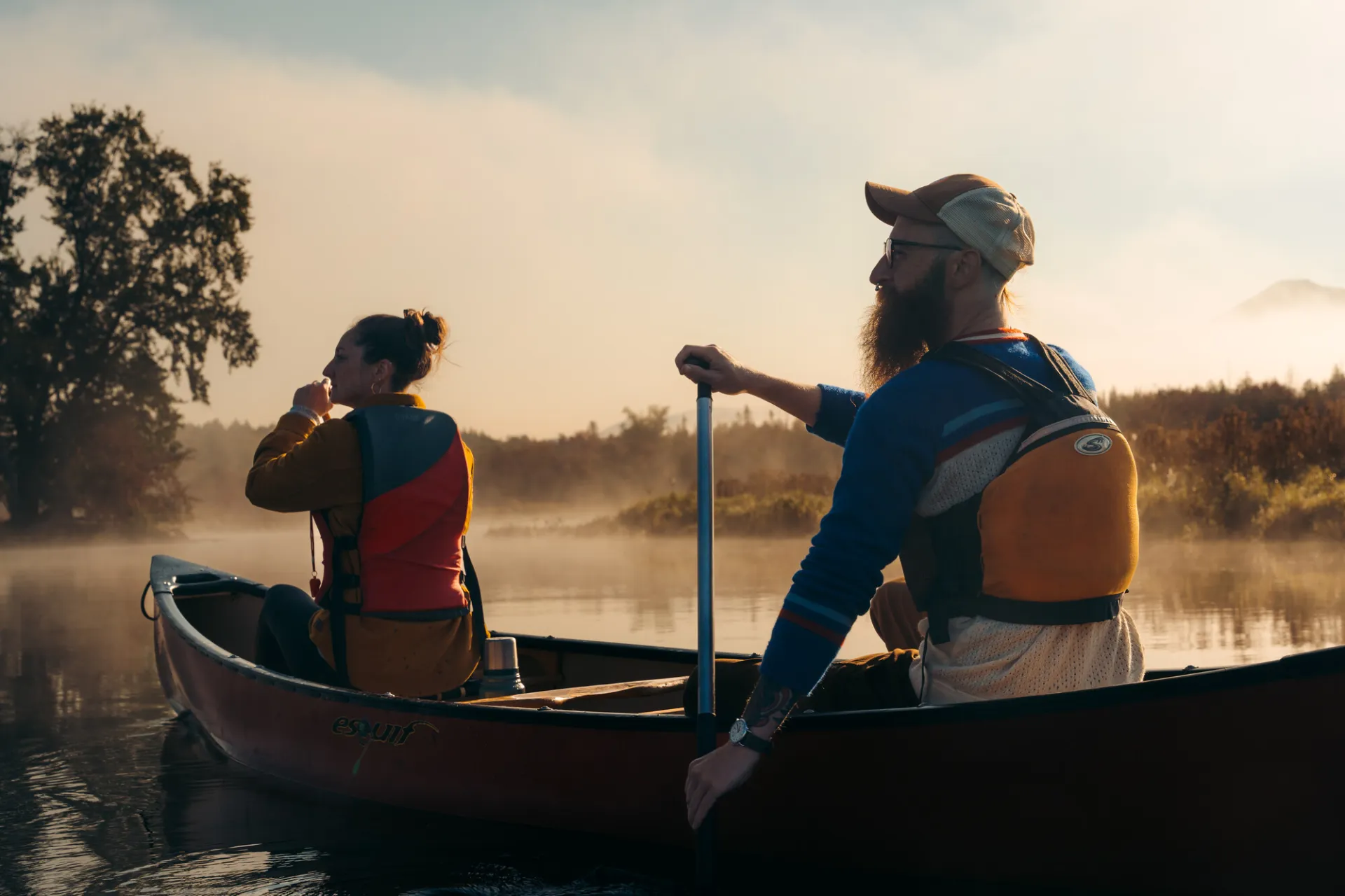 A woman and man paddle a canoe in the low, golden light of sunset.